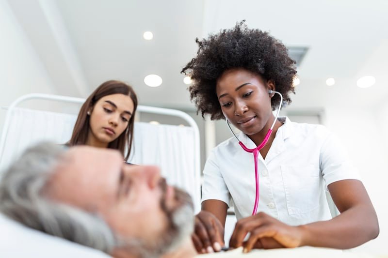 Doctor with stethoscope caring for elderly patient in a hospital bed